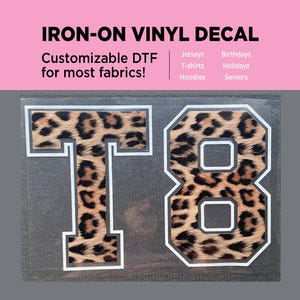 May include: An iron-on vinyl decal featuring the letter T and the number 8 in a varsity-style font with a leopard print pattern. The decal has a white outline and is displayed on a gray background with text that reads IRON-ON VINYL DECAL.