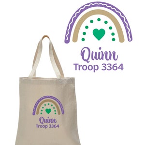 May include: A beige canvas tote bag with a purple and brown rainbow design, a green heart, and the text "Quinn Troop 3364".