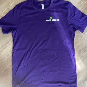 May include: Purple t-shirt with a green heart and the text "TROOP 127066" in white.