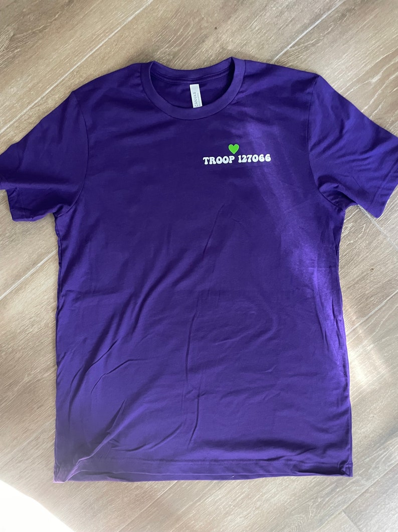 May include: Purple t-shirt with a green heart and the text "TROOP 127066" in white.
