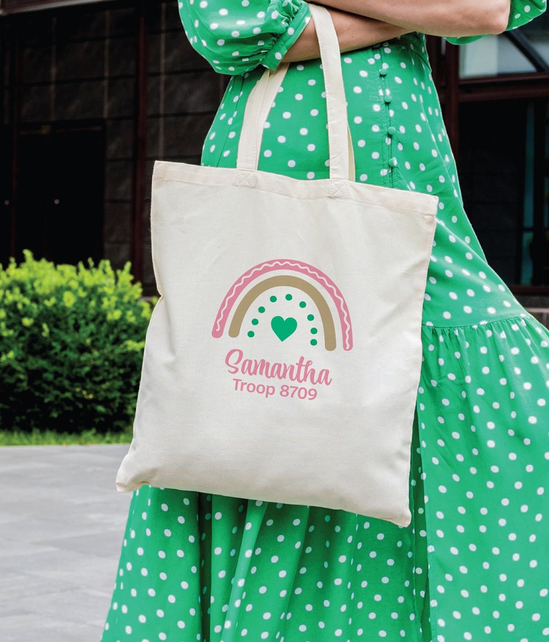 May include: A white canvas tote bag with a rainbow design and the text "Samantha Troop 8709". The rainbow is in shades of pink, brown, and gold with a green heart in the center.