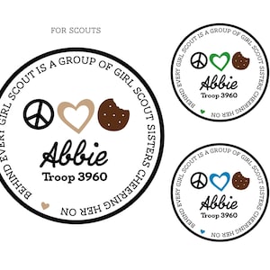 May include: Circular Girl Scout design with a peace sign, heart, and cookie graphic. The text reads "Every Girl Scout is a Group of Girl Scout Sisters Cheering Her On" and includes the name "Abbie" and "Troop 3960".