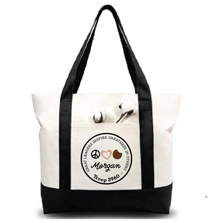 May include: A white canvas tote bag with black accents on the bottom and straps. The front pocket features a circular design with the words "GREAT LEADERS INSPIRE GREATNESS IN OTHERS," the name "Morgan," and "Troop 3960."