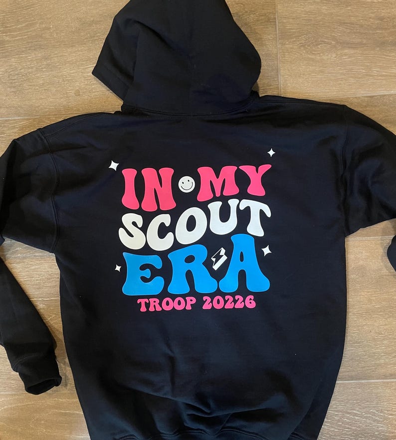 May include: Black hooded sweatshirt with a pink, white, and blue graphic that says "In My Scout Era" with a smiley face and a lightning bolt. The text "Troop 20226" is below the graphic.