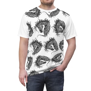 Puede incluir: Camiseta blanca con un patrón repetido de ilustraciones de caballos negros y grises. Los caballos están estilizados con detalles intrincados, creando un diseño único. La camiseta tiene mangas cortas y cuello redondo.