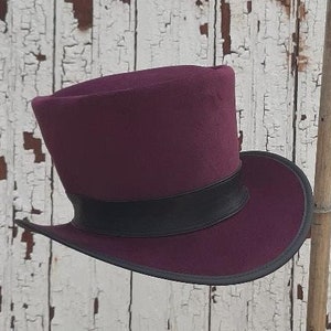 May include: A burgundy top hat with a black band. The hat is made of felt and has a wide brim.