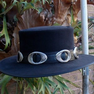 May include: A black felt fedora hat with a wide brim and a silver metal band with decorative accents. The hat has a tall crown.