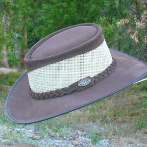 Peut inclure: Un chapeau en cuir marron avec une bande en paille tress&eacute;e et une tresse en cuir autour de la couronne. Le chapeau a une bande en cuir marron avec le texte "COBB & CO" en lettres dor&eacute;es.