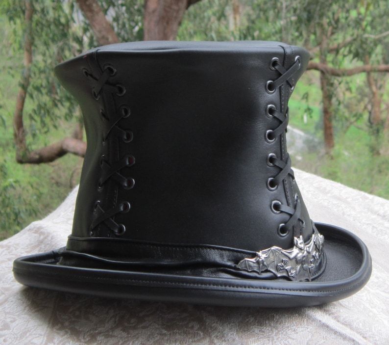 May include: A black leather top hat with a lace-up detail and a silver bat design on the brim.