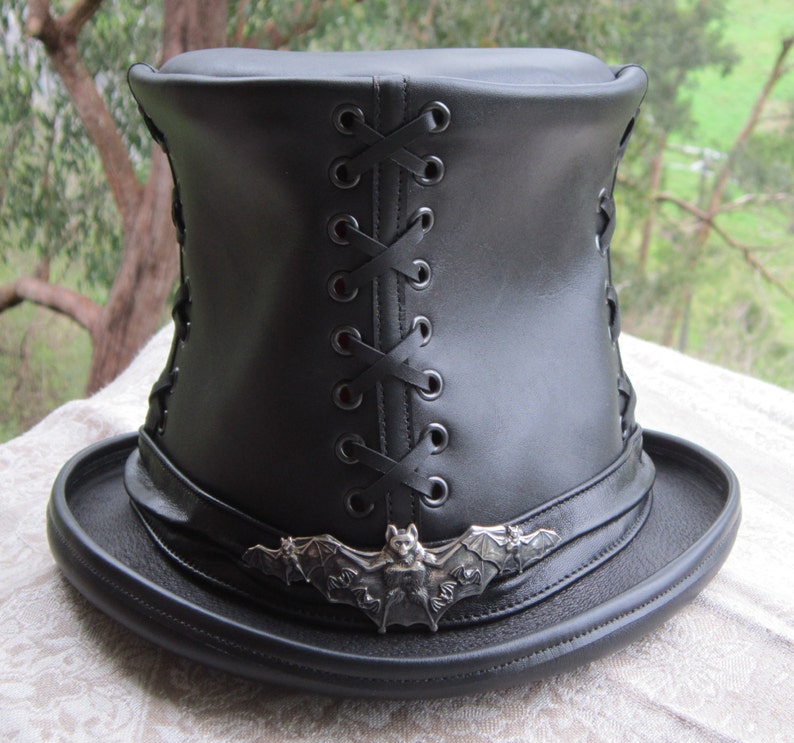 May include: A black leather top hat with a bat design on the front and a lace-up back.