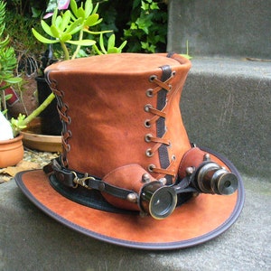 May include: A brown leather top hat with a black lace-up detail and two brass-colored telescopes attached to the brim.