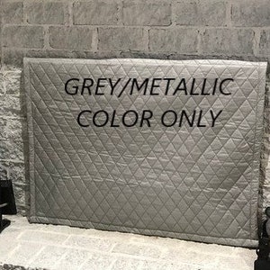 May include: A quilted fireplace screen in a grey metallic color. The screen has a diamond pattern and is designed to protect a fireplace from sparks.