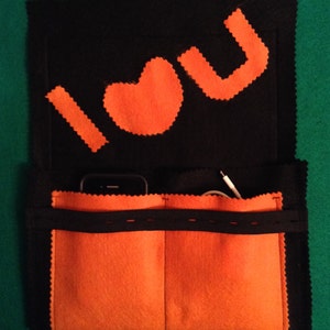 May include: A black felt pouch with orange felt pockets and a black elastic band. The front of the pouch has the words "I love you" written in orange felt.
