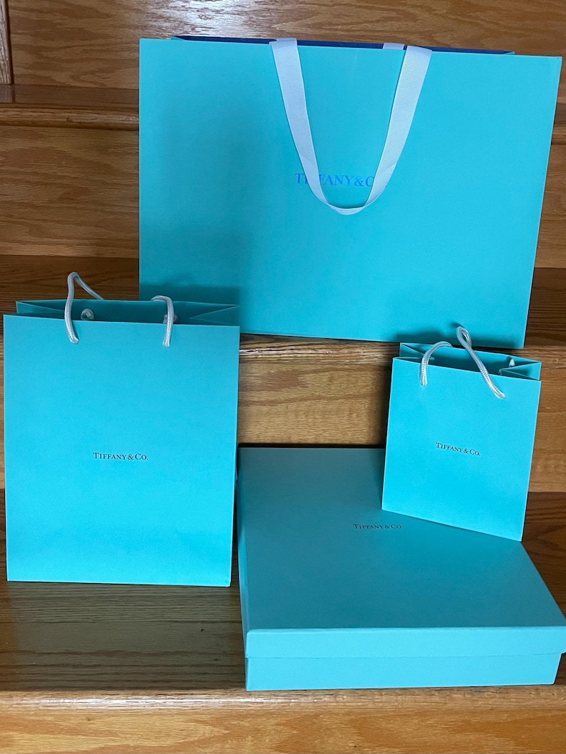 May include: A collection of Tiffany & Co. gift boxes and bags in a signature robin's egg blue. The set includes various sizes of shopping bags with white handles and a rectangular box. The Tiffany & Co. logo is visible on each item.