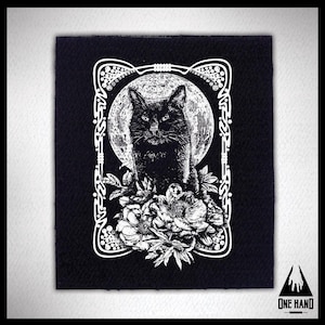 Puede incluir: Parche bordado en blanco y negro con un gato negro sentado frente a una luna llena con flores. El gato está rodeado de un marco decorativo.
