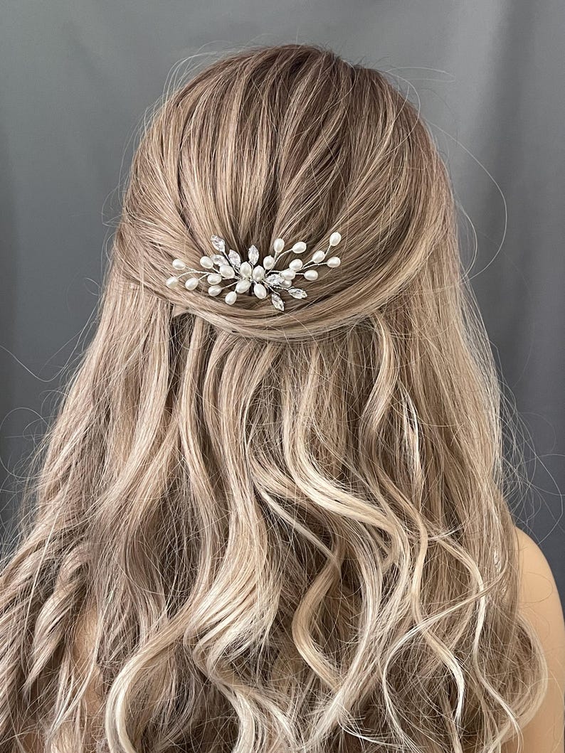 May include: A silver hair comb with pearl and crystal accents. The comb is designed in a delicate floral shape.