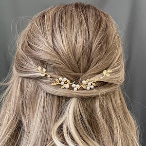 Könnte beinhalten: Ein goldfarbenes Haaraccessoire mit einem filigranen Design aus Blättern und kleinen, runden Perlen. Das Haarteil ist im Haar platziert und verleiht einen Hauch von Eleganz. Das Accessoire ist zum Tragen im Haar bestimmt.