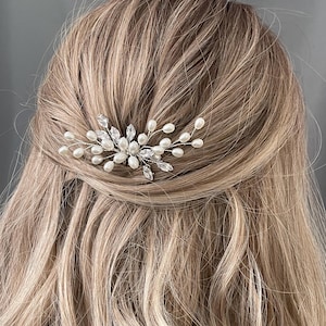 May include: A silver hair comb with white pearls and clear rhinestones. The comb is designed to look like a delicate floral branch.