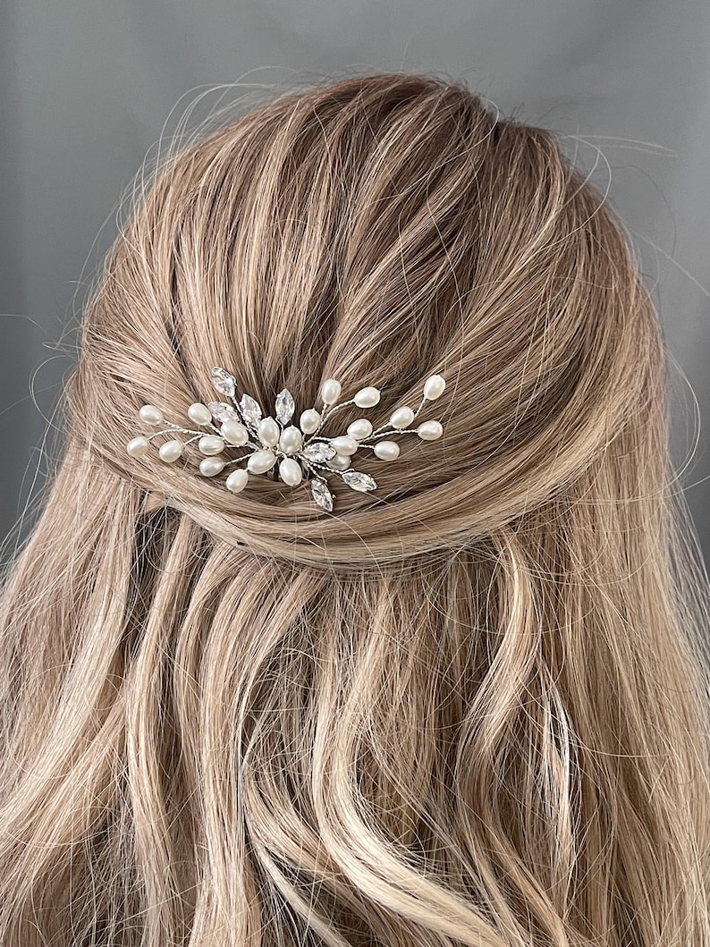 May include: A silver hair comb with white pearls and clear rhinestones. The comb is designed to look like a delicate floral branch.