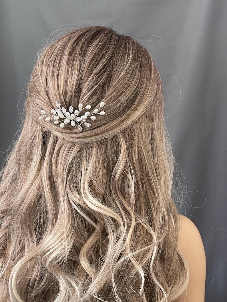 May include: A pair of silver hair clips with pearl and crystal embellishments. The clips are arranged in a delicate, floral design.