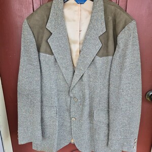 May include: A gray tweed blazer with brown suede elbow patches. The blazer has a single button closure and two pockets.