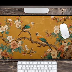 May include: A rectangular mouse pad featuring a golden background with a floral and bird design. Two birds with blue, orange, and yellow plumage perch on a branch with white and pink flowers. A white mouse is on the right.