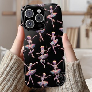 May include: Black phone case featuring a repeating pattern of skeleton ballerinas in tutus. The skeletons are in various ballet poses, with iridescent accents. The case has a glossy finish and a camera bump.
