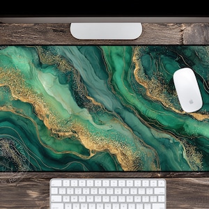 May include: A rectangular mouse pad with a vibrant abstract design in shades of green and gold. The design features flowing, marbled patterns with gold accents. A white computer mouse rests on the pad, with a keyboard and monitor visible.