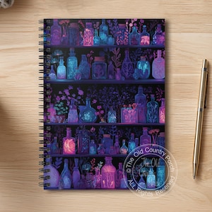 May include: A spiral-bound notebook featuring a colorful illustration of shelves filled with glass bottles and jars in shades of purple, blue, and pink. The notebook has a dark background and a gold pen is placed on the wooden surface.