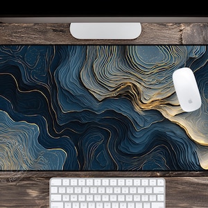 May include: A rectangular mouse pad with a blue and gold abstract design. The pattern resembles layered topography with flowing lines. A white computer mouse rests on the pad, with a white keyboard below.