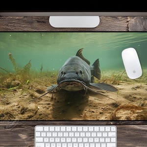 May include: A rectangular desk mat featuring an underwater scene with a large fish. The fish is dark gray with long barbels and fins, set against a sandy bottom and clear water. A white computer mouse is visible.