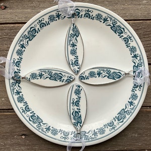 Puede incluir: Cuatro adornos ovalados con un diseño floral blanco y verde azulado, dispuestos sobre un plato blanco con un borde floral verde azulado. Cada adorno tiene un alambre plateado y una cinta blanca transparente para colgar. Un artículo de decoración del hogar único.