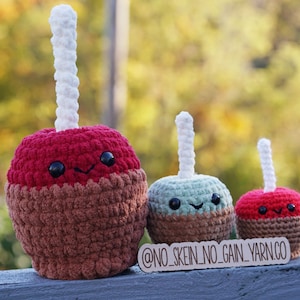 May include: Three crocheted candy apples, one red, one green, and one red, with white sticks. The apples are smiling and have black eyes. The largest apple is on the left, the smallest on the right. The caption at the bottom reads "@NO_SKEIN_NO_GAIN_YARN.CO"