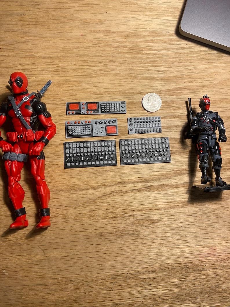 May include: Two Deadpool action figures, one in a red and black suit and the other in a grey and black tactical suit. Several small grey and black computer-like components are also present, along with a US quarter.