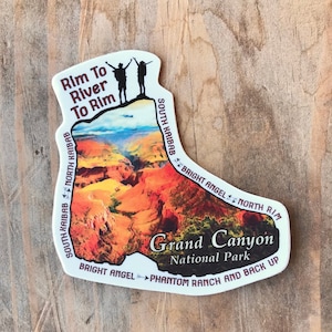 May include: A sticker in the shape of a boot, featuring a colorful depiction of the Grand Canyon. The sticker includes text that reads "Rim To River To Rim" and "Grand Canyon National Park". Two silhouettes of people are at the top.