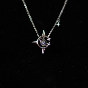 May include: A silver necklace with a star pendant featuring a small globe inside a crescent moon. The pendant is surrounded by three smaller stars.