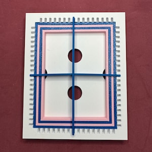 May include: A white, rectangular object with a blue and pink frame design. Two dark red circles are visible within the white space. A blue grid pattern overlays the frame. The outer edge has a series of small, vertical lines.