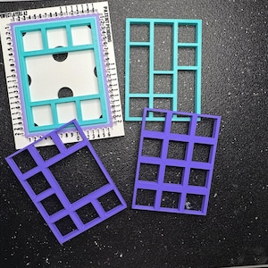 May include: Three rectangular plastic grid frames in teal and purple, featuring various internal compartment layouts. One teal frame is positioned on a white measuring guide labeled Perfect Layers A2 with numerical markings in inches.