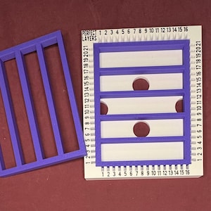 May include: A purple rectangular frame with five vertical bars sits next to a white and purple tool with the text "PERFECT LAYERS" and numbered markings. The tool has five rectangular cutouts with circular holes.