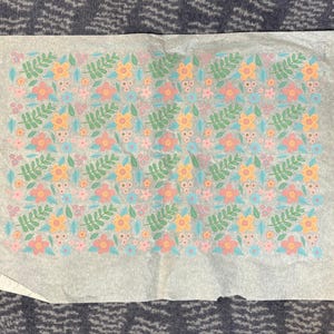 May include: A sheet of parchment paper with a repeating floral pattern. The design features pink, yellow, and blue flowers, along with green leaves, set against a light background. The edges of the paper are torn.