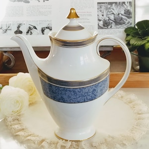 May include: A white porcelain teapot with a blue and gold patterned design. The teapot has a gold lid with a gold knob.