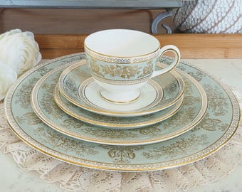 May include: A vintage tea set with a light blue and gold floral design. The set includes a teacup, saucer, and plates of varying sizes. The edges are trimmed with gold. The set is placed on a lace doily.