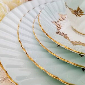 May include: A set of light blue porcelain plates and a teacup with gold detailing. The plates have a fluted design and gold rims. The teacup and saucer feature gold leaf patterns. A classic and elegant tea set.
