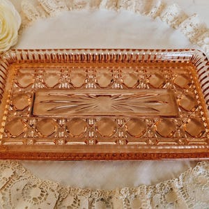 May include: A vintage pink glass serving tray with a raised, geometric design. The tray is rectangular in shape and has a slightly raised edge.