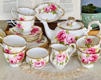 May include: A complete vintage tea set with a white teapot, cups, saucers, and serving dish, decorated with pink rose patterns and gold edging. Includes a creamer and sugar bowl. A classic tea set for a traditional afternoon tea.