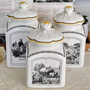 Puede incluir: Tres botes de cerámica blanca con tapas rematadas por flores amarillas y blancas. Cada bote presenta una escena pastoral en blanco y negro, un borde de hojas negras y una línea decorativa amarilla. Los recipientes cuadrados muestran ilustraciones detalladas de la vida rural.