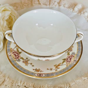 May include: A white porcelain soup bowl with handles, on a matching saucer. The saucer and bowl have a floral design with gold trim. The design includes pink, blue, and gold accents. A classic tea set.