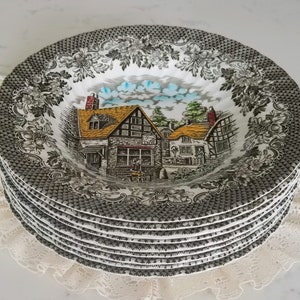 May include: A stack of six vintage soup bowls. Each bowl has a black and white floral and geometric border design. The centre of each bowl displays a colourful village scene with a yellow-roofed building and blue sky.