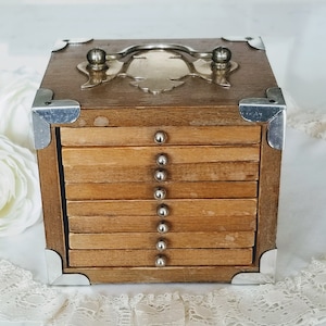 以下が含まれることがあります： シルバーのハンドルとコーナーアクセントが付いた木製のコースターセット。セットには、それぞれシルバーのスタッドが付いた木製コースターのスタックが含まれています。ボックスは正方形で、上部に装飾的なシルバープレートが付いています。