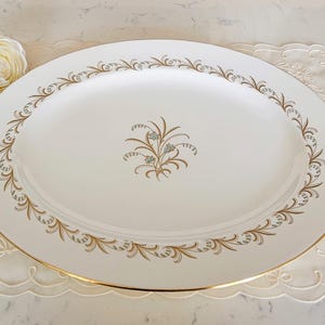 Puede incluir: Plato ovalado para servir con fondo blanco y ribete dorado. El borde presenta un diseño floral dorado y marrón. Un diseño floral más pequeño está centrado en el plato. El plato mide unos 40 cm de largo.